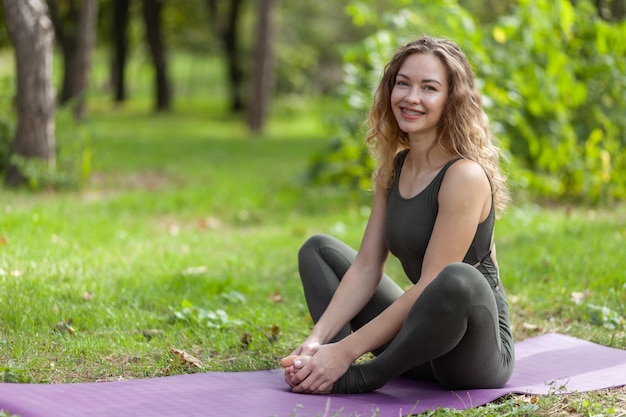 Glückliche kaukasische Yogifrau, die auf einer Matte auf dem Gras sitzt Gesunder Lebensstil