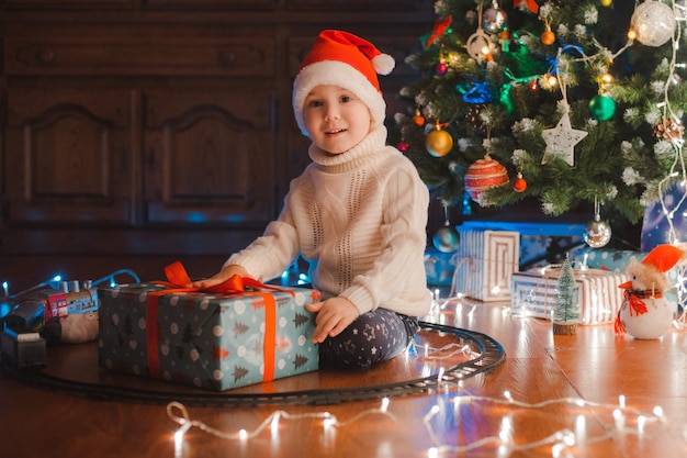 Glückliche Kinder des kleinen Jungen in Sankt-Hut mit Geschenk haben Weihnachten oder neues Jahr.