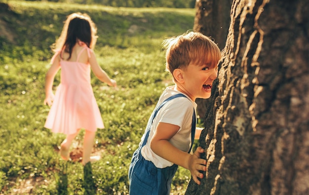 Glückliche Kinder, die draußen zusammen spielen Netter kleiner Junge und kleines Mädchen, die lachen und Spaß im Park haben Fröhliche Kinder, die im Freien Verstecken spielen Aktivitäten draußen mit Kindern Kindheit