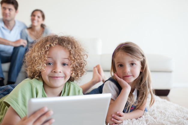 Glückliche Kinder, die einen Tablet-Computer verwenden, während ihre glücklichen Eltern aufpassen