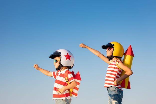 Glückliche Kinder, die mit Spielzeugrakete gegen Sommerhimmelhintergrund spielen