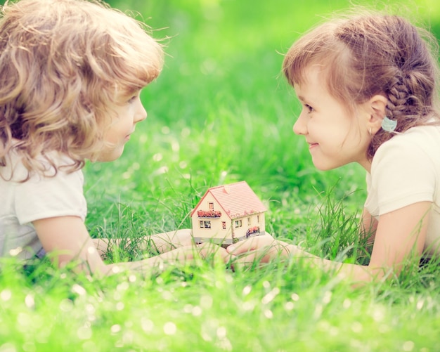 Foto glückliche kinder, die musterhaus in den händen halten kinder, die auf grünem gras im frühlingspark liegen neues hauptkonzept