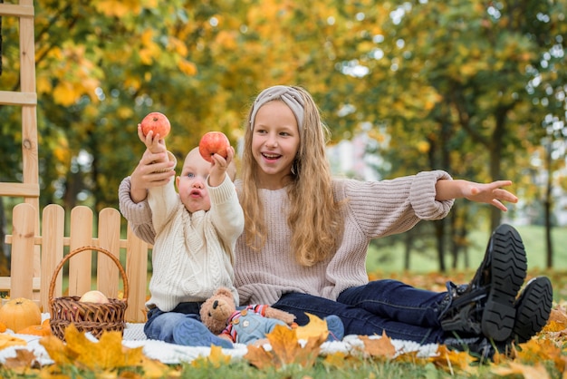 Glückliche Kinder, die roten Apfel essen, während sie im Herbstpark gehen.