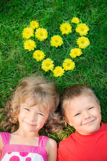 Glückliche Kinder, die Spaß im Freien haben Herzform Frühlingsblumen Junge und Mädchen liegen auf grünem Gras Ferienkonzept Valentinstag