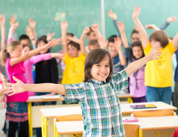 Glückliche Kinder gruppieren mit den Armen, die im Schulklassenzimmer ausgestreckt werden