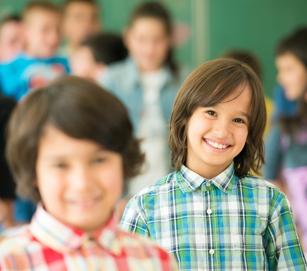 Glückliche Kinder gruppieren mit den Armen, die im Schulklassenzimmer ausgestreckt werden