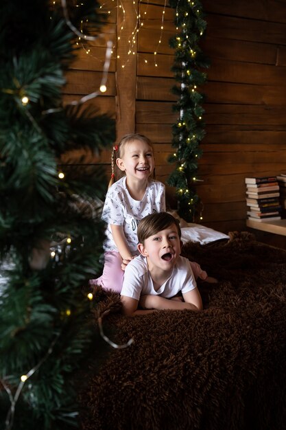 Glückliche Kinder im Pyjama, die am Weihnachtsmorgen in der Nähe des Weihnachtsbaums spielen