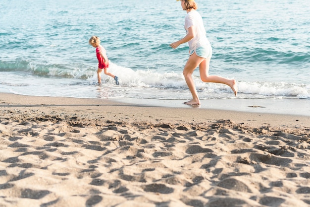 Glückliche Kinder im Urlaub am Meer, die im Wasser laufen, Junge und Mädchen, die im Sommer am Strand spielen ...