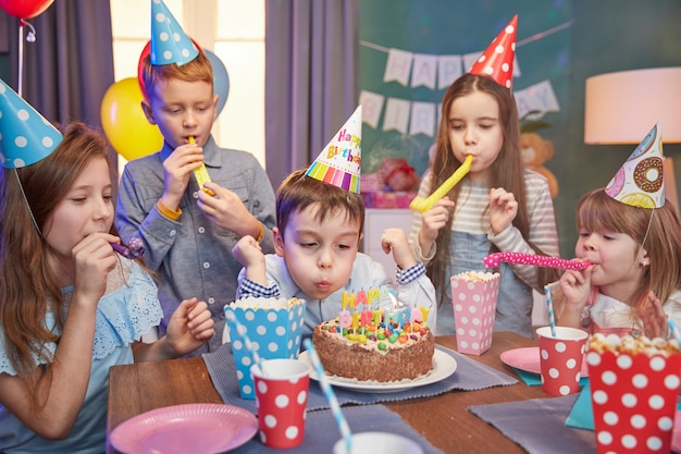 Glückliche Kinder in den Partykappen, die einen Geburtstag feiern