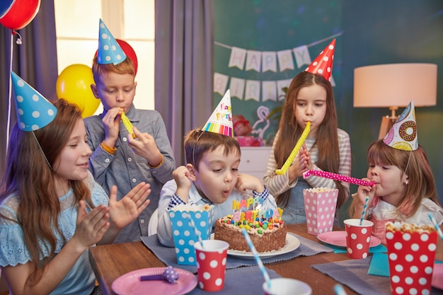 Glückliche Kinder in den Partykappen, die einen Geburtstag feiern