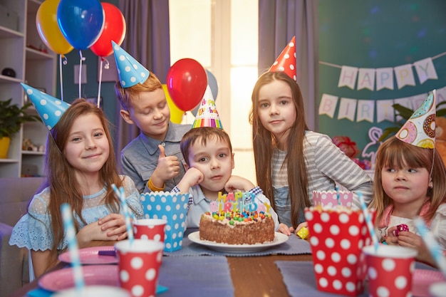 Glückliche Kinder in den Partykappen, die einen Geburtstag feiern