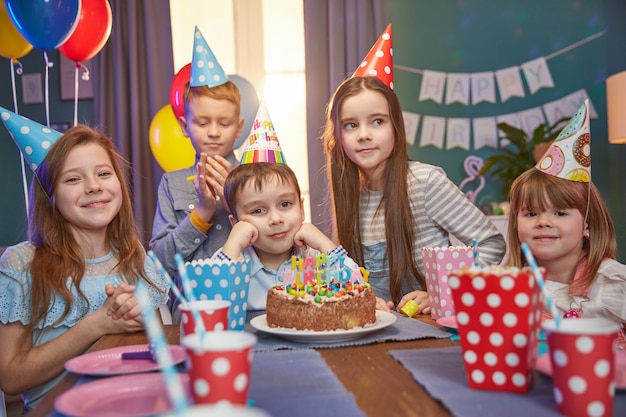 Glückliche Kinder in den Partykappen, die einen Geburtstag feiern