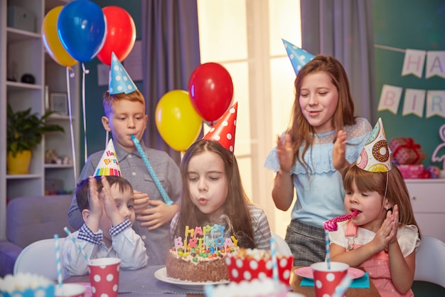 Glückliche Kinder in den Partykappen, die einen Geburtstag feiern