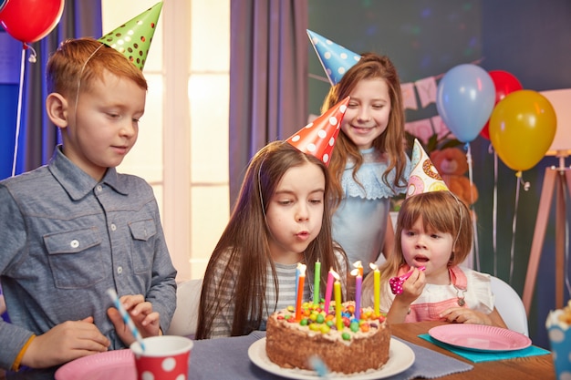 Glückliche Kinder in den Partykappen, die einen Geburtstag feiern