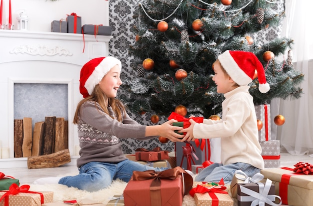 Glückliche Kinder in Weihnachtsmützen, die Weihnachtsgeschenke auspacken