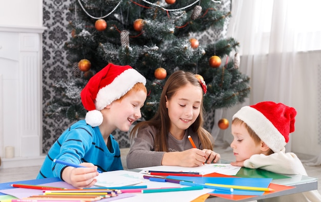 Glückliche Kinder in Weihnachtsmützen machen Wunschliste von Weihnachtsgeschenken