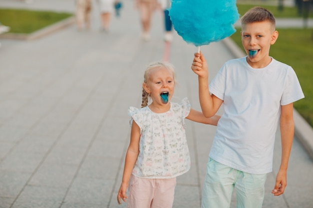 Glückliche Kinder, Junge und Mädchen, die draußen blaue Zuckerwatte essen.