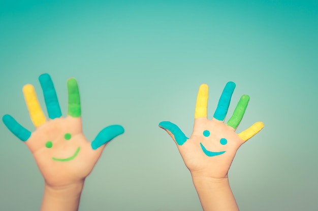 Glückliche Kinder mit Smiley auf den Händen vor blauem Sommerhimmel