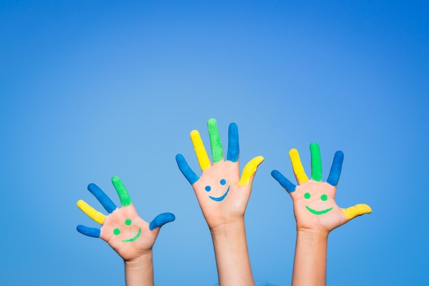 Glückliche Kinder mit Smiley auf Händen gegen blauen Sommerhimmelhintergrund