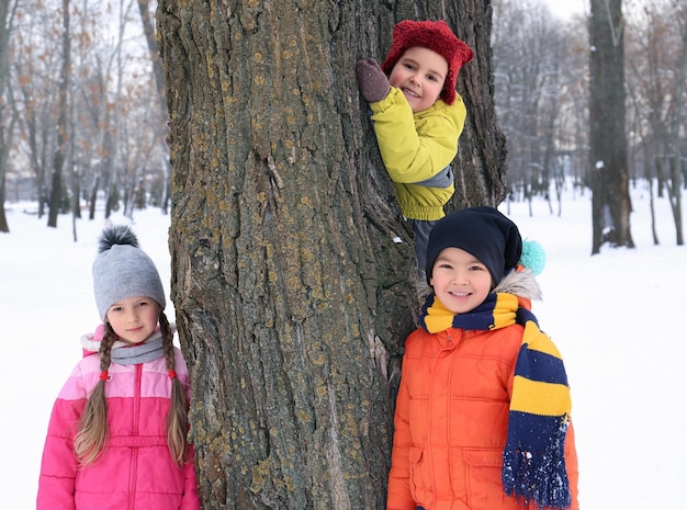 Glückliche Kinder nahe Baum im verschneiten Park im Winterurlaub