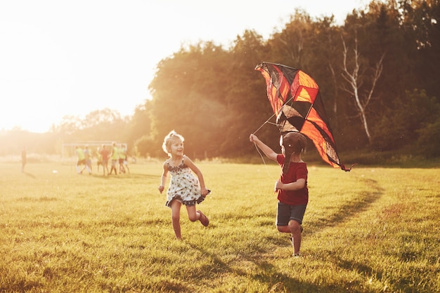 Glückliche Kinder starten bei Sonnenuntergang einen Drachen auf dem Feld. Kleiner Junge und Mädchen in den Sommerferien