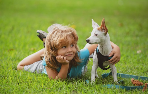 Glückliche Kinder- und Hundeumarmungen, die auf dem Rasen im Hinterhof liegen. Nettes Jungenkind mit dem Hund, der auf Park sich entspannt. Welpen und Kind im Gras im Freien.