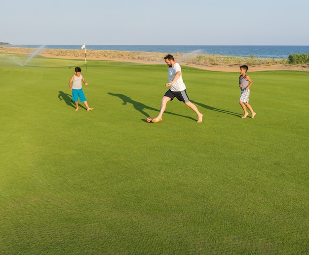 Glückliche Kinder und Vati auf dem Sommergolfgrasgelände, das den Spaß und glückliche Zeit spielt Fußball hat