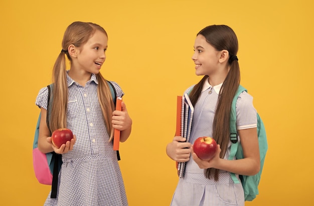 Glückliche Kinderfreunde zurück zur Schule, die Bücher und Äpfel für eine gesunde Ernährung auf gelbem Hintergrund halten