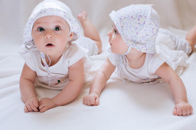 Glückliche Kinderzwillinge in den lustigen Hüten auf einem weißen Hintergrund