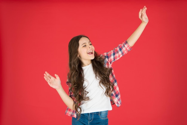 Glückliche Kindheit Kindermode Kleines Mädchen mit schönen langen Haaren Kindertag Glückliches kleines Mädchen auf rotem Hintergrund Kleines Mädchen tanzt Little cutie Lächelndes Mädchen zum Ausdruck bringen Positivität Hier bin ich