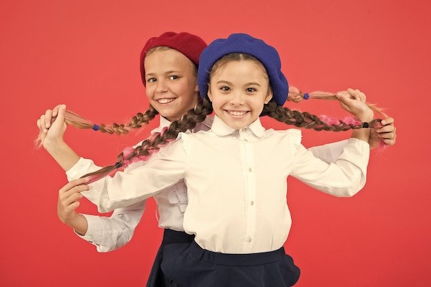 Glückliche Kindheit Nette Kinder auf rosa Hintergrund Kleine Kinder, die geflochtenes Haar in langen Zöpfen halten Kleine Kinder, die Schuluniform und Baskenmützen tragen Adorable Schulkinder mit Mode-Look