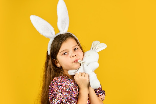 Glückliche Kindheit. süßes kinderspiel mit spielzeug. Spielzeugladenkonzept. Mädchen in lustigen Hasenohren. frohe osterferien. Vorbereitung auf die Frühlingsferien. Osterhasenkind. kleines Mädchen hält Hasenspielzeug gelber Hintergrund.