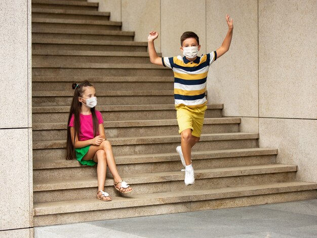 Glückliche kleine kinder, die eine schützende gesichtsmaske tragen, springen und laufen auf der stadtstraße. sieht glücklich, fröhlich, aufrichtig aus. exemplar. kindheit, pandemiekonzept. gesundheitswesen, coronavirus-pandemie.