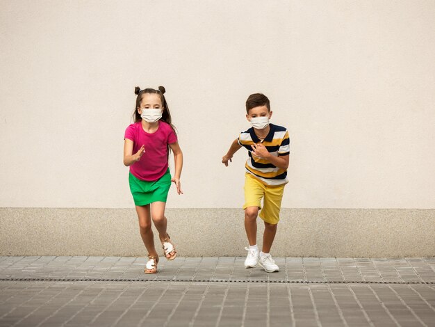 Glückliche kleine Kinder, die eine schützende Gesichtsmaske tragen, springen und laufen auf der Stadtstraße. Sieht glücklich, fröhlich, aufrichtig aus. Exemplar. Kindheit, Pandemiekonzept. Gesundheitswesen, Coronavirus-Pandemie.