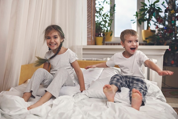 Glückliche kleine Kinder im Pyjama springen im Bett im Schlafzimmer