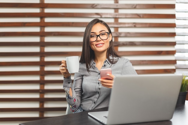 Glückliche lächelnde Frau, die mit Laptop arbeitet und Kaffee trinkt