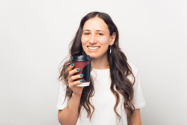 Glückliche lächelnde Frau hält eine Tasse Kaffee zum Mitnehmen.