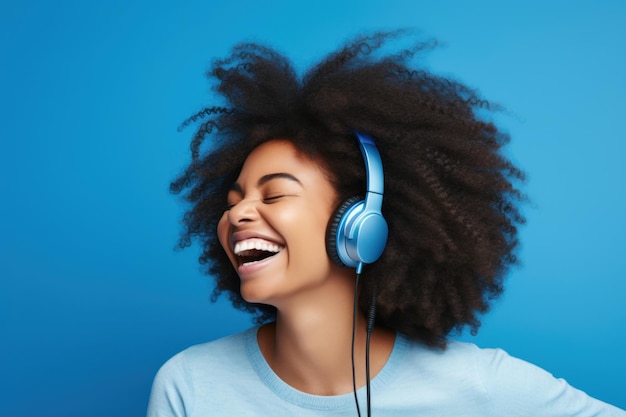Foto glückliche lächelnde frau mit afro-krulligem haar und kopfhörern lachendes weibliches modell hört musik auf blauem pastellfarbenem hintergrund
