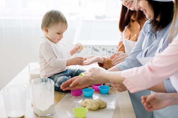 Foto glückliche lächelnde frauen, die zusammen mit dem kleinen baby zu hause küche, muttertag, familienkonzept backen. frauen geben teig in farbige silikon-backbecher für muffins