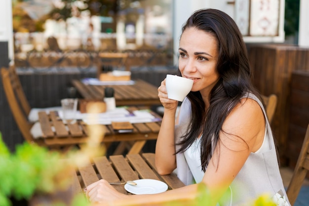 Glückliche lächelnde Geschäftsbrünette trinkt Kaffee in einem Straßencafé Kaffeepause Lifestyle-Konzept