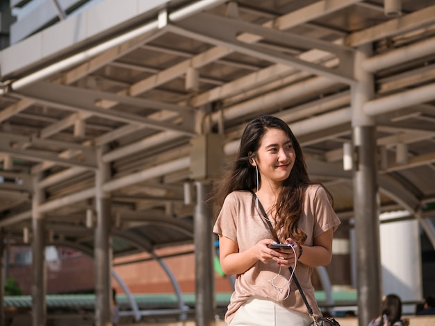 Glückliche lächelnde junge asiatische Frau hört Musik im Kopfhörer und benutzt Smartphone.