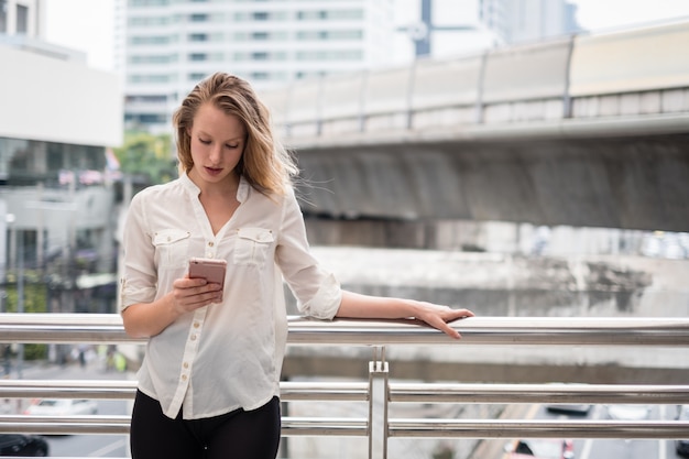 Glückliche lächelnde junge Frau, die Telefon in der Stadt mit Raum für Text verwendet