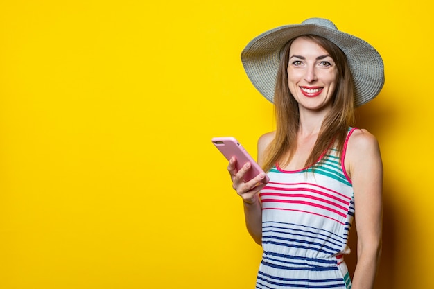 Glückliche lächelnde junge Frau im Hut und im gestreiften Kleid, die Telefon hält und aufwirft