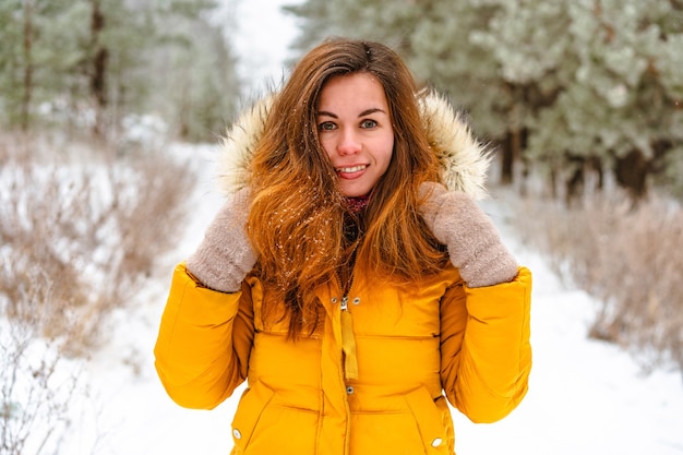 Glückliche lächelnde junge Frau in der gelben Jacke im verschneiten Winterwald