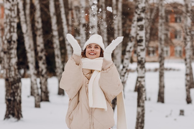 Glückliche lächelnde junge Frau, Porträt, gekleideter Mantel, Schal, Hut und Handschuhe genießt das Winterwetter im schneebedeckten Winterpark