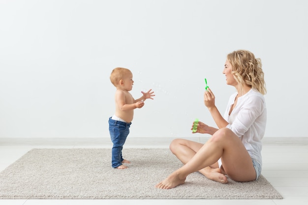 Glückliche lächelnde junge mutter, die mit kleinem baby zu hause spielt