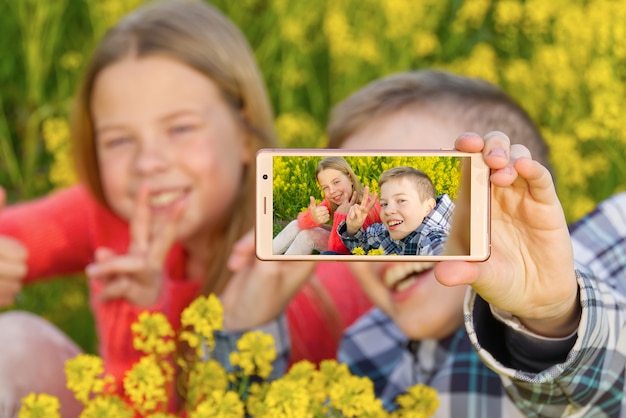 Glückliche lächelnde Kinder, die Selbstporträt auf Smartphone in Wiese machen.