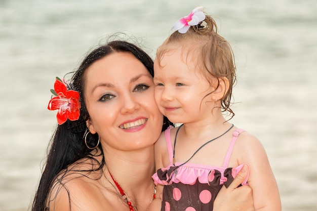 Glückliche lächelnde Mutter mit einem Tochterkind spielt am Strand und baut Sandburgen an einem sonnigen Sommer d