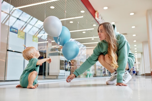 Foto glückliche lächelnde mutter mit ihrem baby kriecht auf dem boden und farbige ballons junge hübsche mutter und