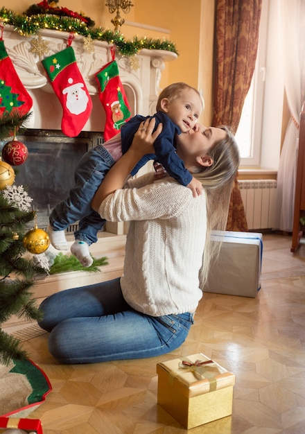 Glückliche lächelnde Mutter und 1-jähriger Babysohn posieren am Weihnachtsbaum